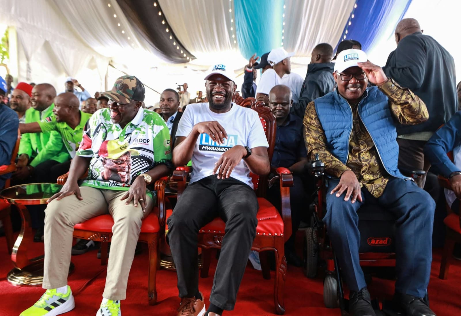 Leaders in Linda Mwananchi shirts and caps sharing a laugh at a rally